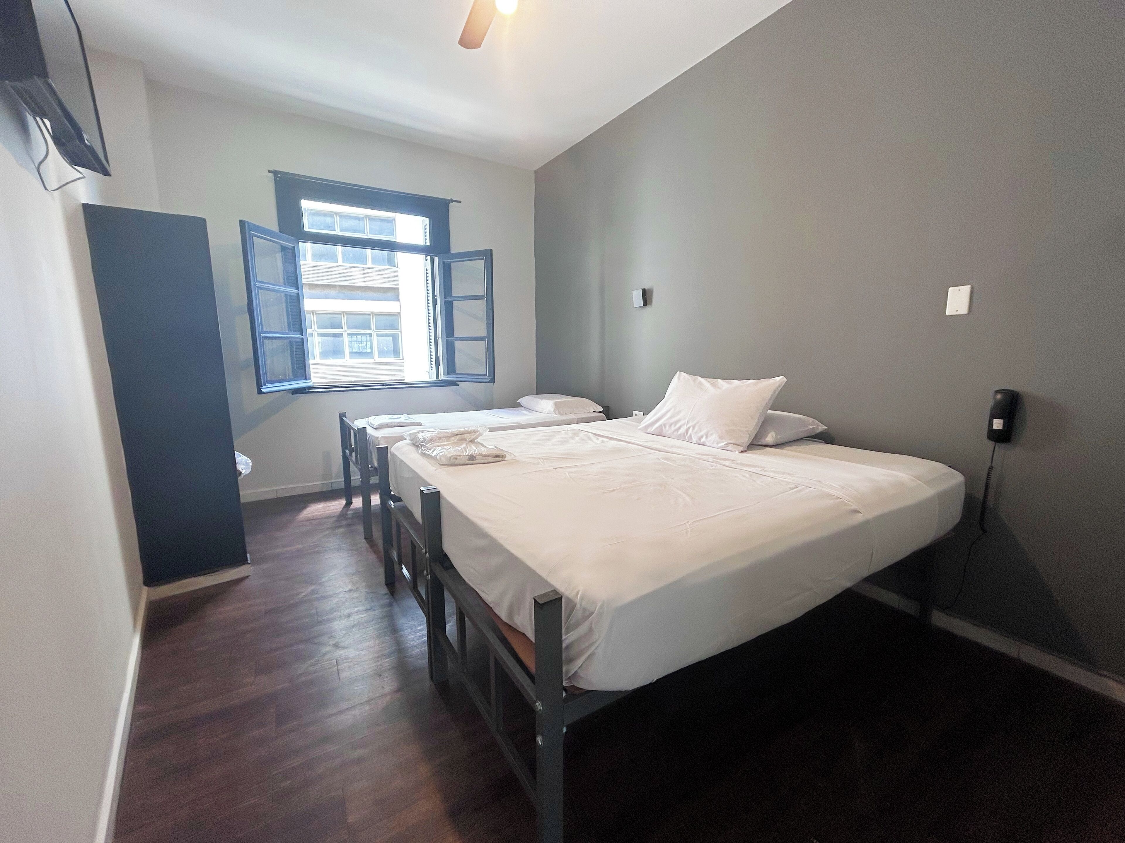 Un dormitorio con cama, una silla, un ventanal y un teléfono en la pared.