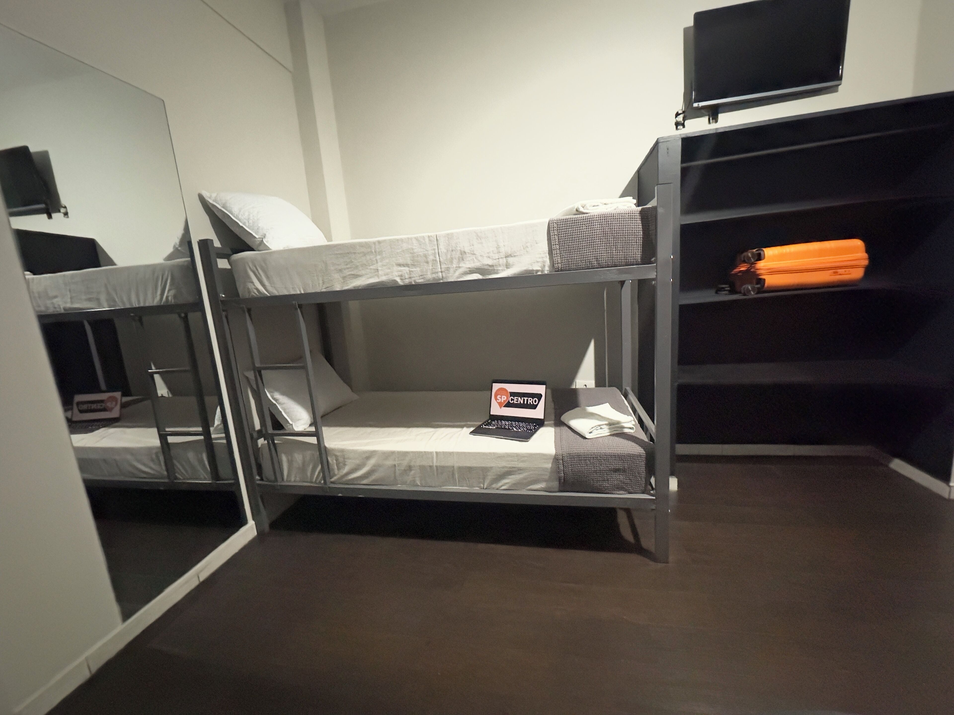 A bunk bed room with a laptop on the lower bunk, a television on the wall, and a suitcase on the upper bunk.