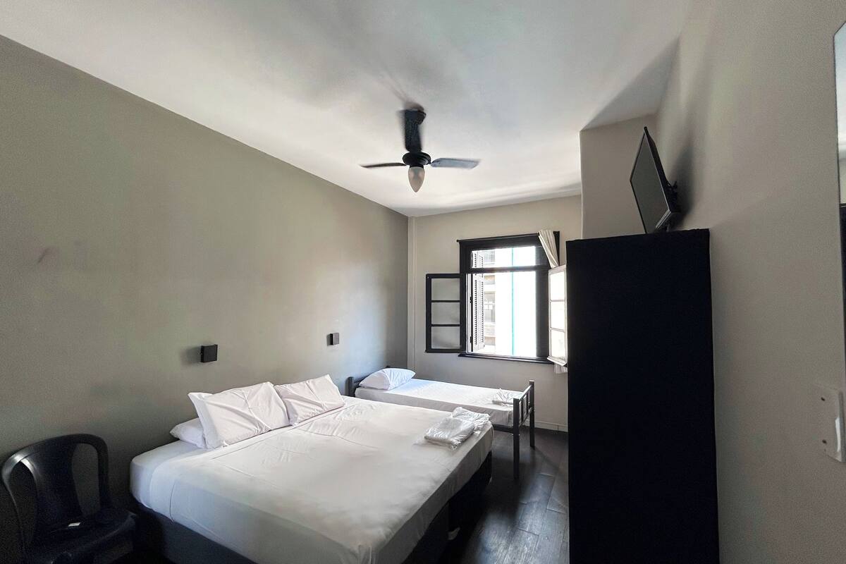 Une chambre d’hôtel avec deux lits, un ventilateur de plafond, une fenêtre avec des rideaux et un bureau.