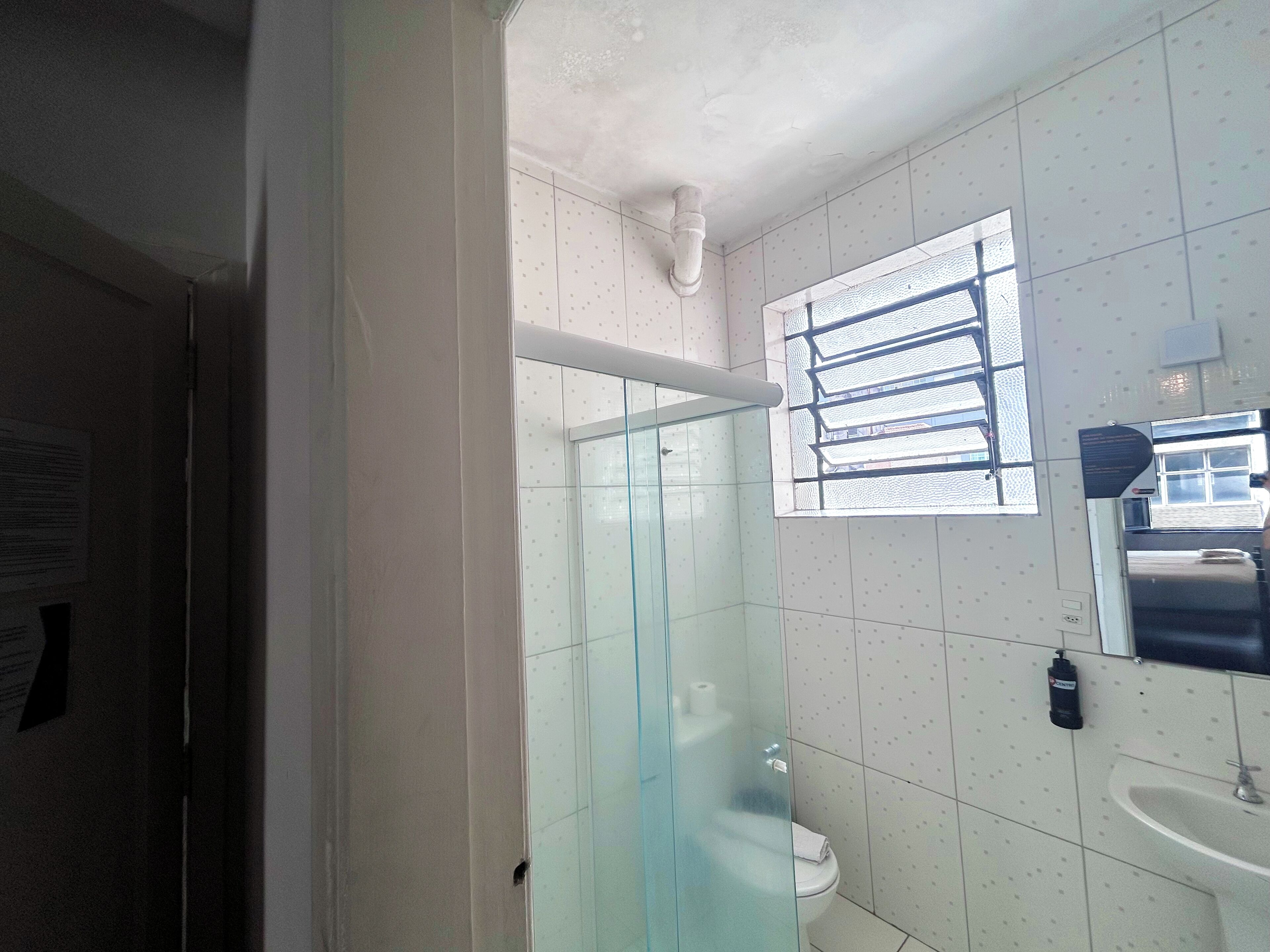 A bathroom with a glass shower enclosure, a toilet, a sink, and a window with blinds.