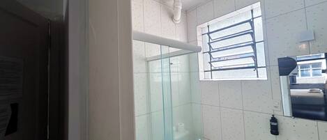 A bathroom with a glass shower enclosure, a toilet, a sink, and a window with blinds.