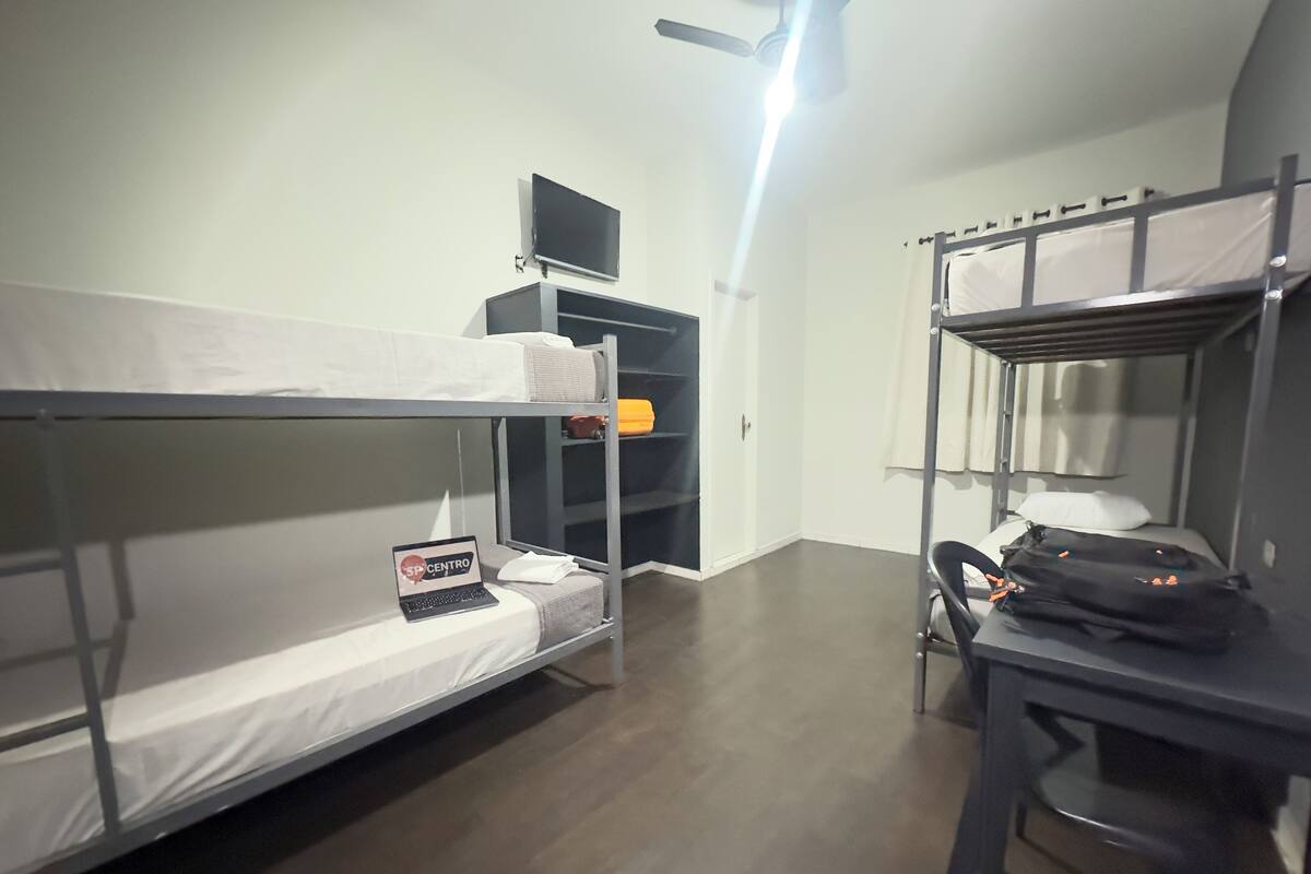 Une chambre avec un lit superposé, un bureau, une étagère avec un ordinateur portable et un ventilateur de plafond.