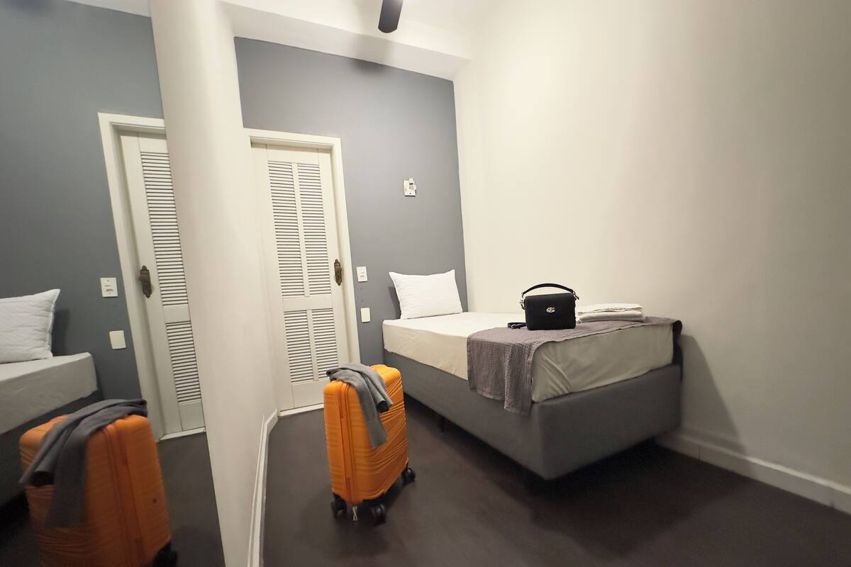 Une petite pièce, de taille modeste, comprenant un lit, une valise et une valise à roulettes.