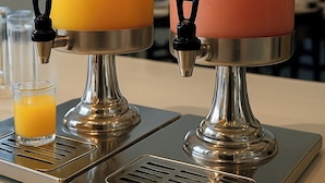 Two stainless steel beverage dispensers with transparent sections, one containing orange juice and the other pink juice, on a countertop. - HOTEL SP CENTRO (São Paulo)