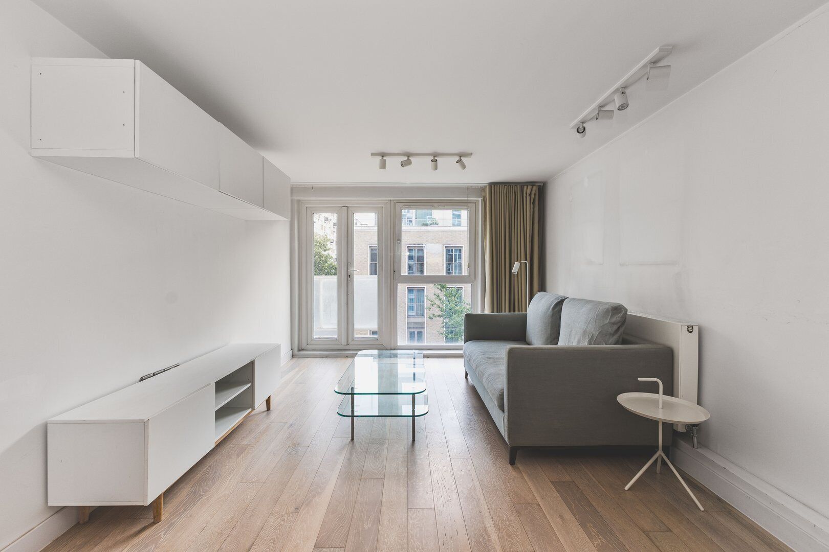 Un salon moderne avec un canapé, une table basse en verre et un meuble de rangement blanc pour appareils multimédias.