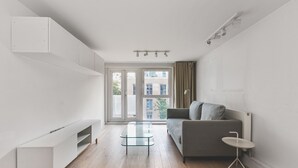 Una sala de estar moderna con un sofá, una mesa de centro de vidrio y un mueble blanco para entretenimiento.