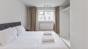 Habitación de hotel moderna con una cama grande, una ventana con cortinas, un radiador y un armario.