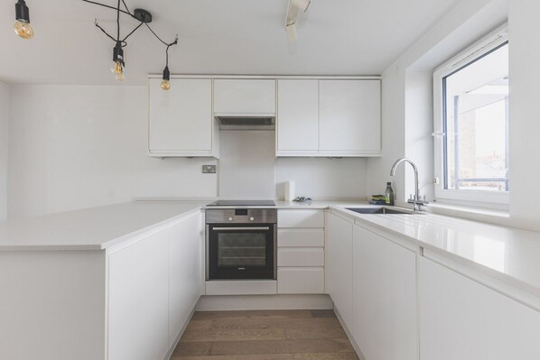 Una cocina moderna con armarios blancos, horno empotrado, lavaplatos e iluminación colgante.