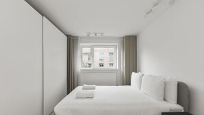 Een moderne hotelkamer met een groot bed, nachtkastje, raam met gordijnen en uitzicht op gebouwen.