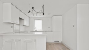 Een moderne keuken met witte kasten, een centraal eiland met barkrukken, een inbouwoven en een hangende lamp.