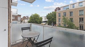 Een balkon met een tafel en stoelen, met uitzicht op een stadsgezicht met gebouwen en een bus.
