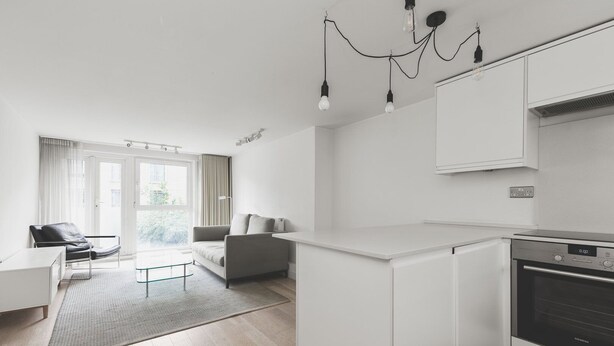 Een moderne keuken met witte kasten, een inbouwoven en een eethoek met een glazen tafel en een bank.