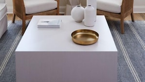 Una sala moderna con dos sillones de mimbre, una mesa de centro blanca y un cuenco dorado.