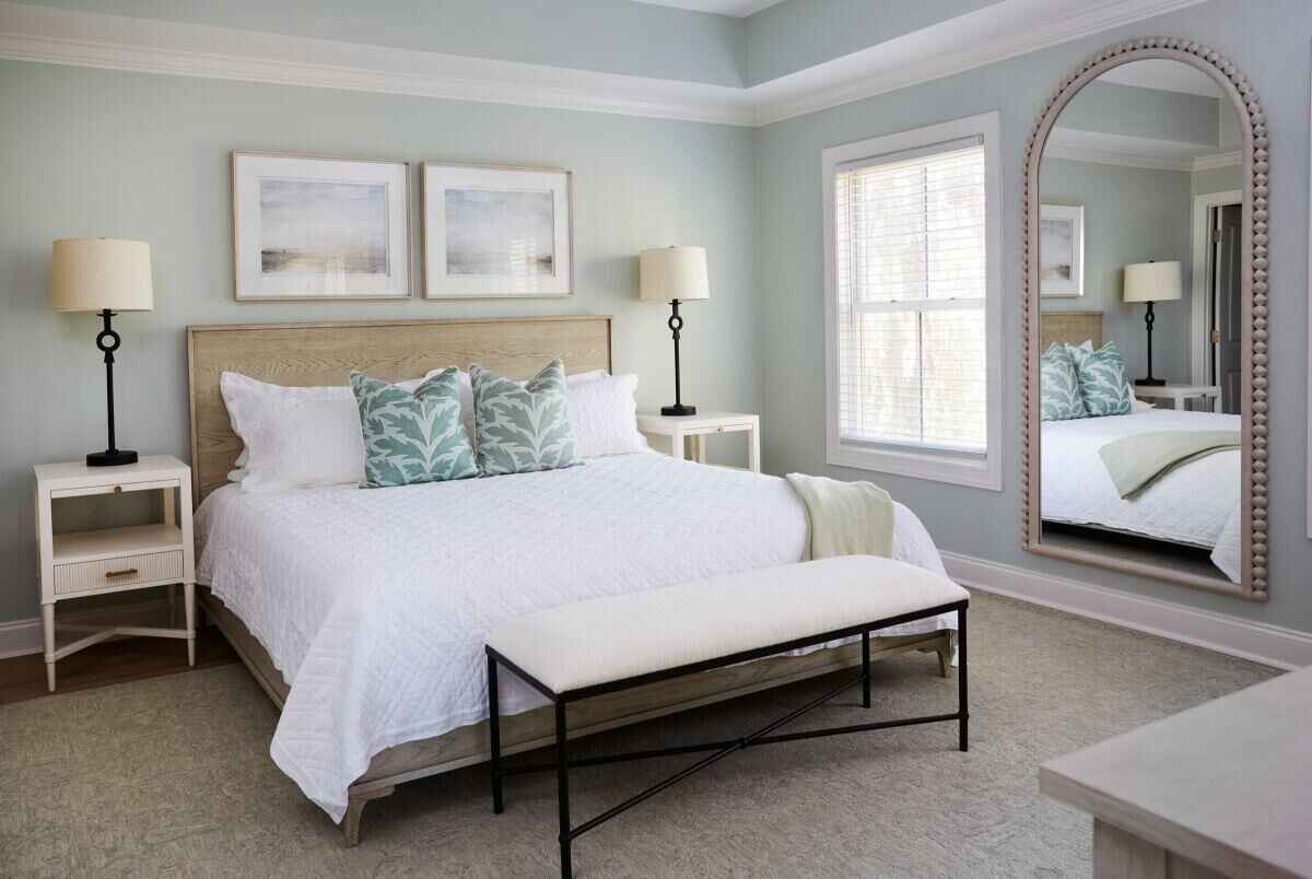 A bedroom with a bed, bedside tables, a bench, a large mirror, and artwork on the wall.