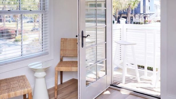 A room with a sliding glass door leading to an outdoor deck, a wicker chair, a small white table, and a window with blinds. - May River Breeze! 3-story Townhouse in Old Town's Promenade (Bluffton)