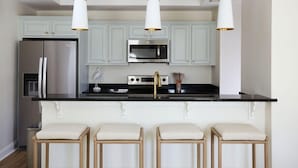 Una cocina moderna con un refrigerador de acero inoxidable, un microondas y una estufa a gas. Hay tres taburetes de bar con asientos acolchados.