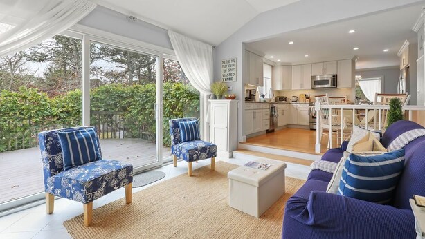 Ein großzügiger Wohnbereich mit einem großen Schiebeglastür zum Balkon, einer Küche im Hintergrund und einem Sofa mit gestreiften Kissen.