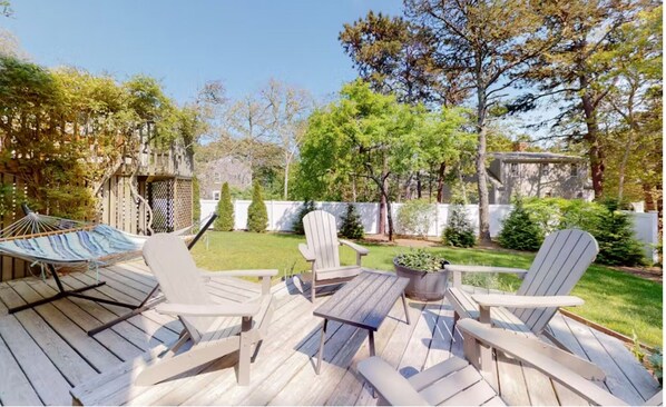 A wooden deck with Adirondack chairs, a hammock, and a small table.