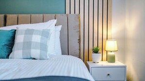 Een keurig opgemaakt bed met kussens, een nachtkastje met lamp en een kleine plant in pot.