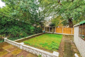 A fenced backyard with a grassy area, a wooden fence, and a building with a window.