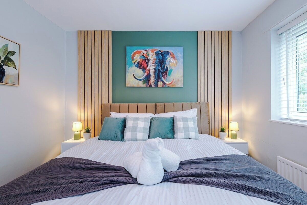 A hotel room with a bed, pillows, a painting, and bedside lamps.