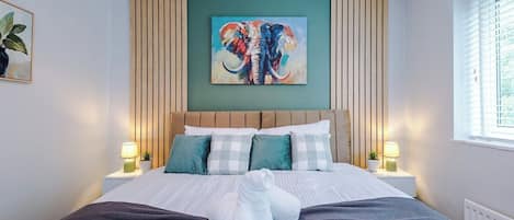 A hotel room with a bed, pillows, a painting, and bedside lamps.