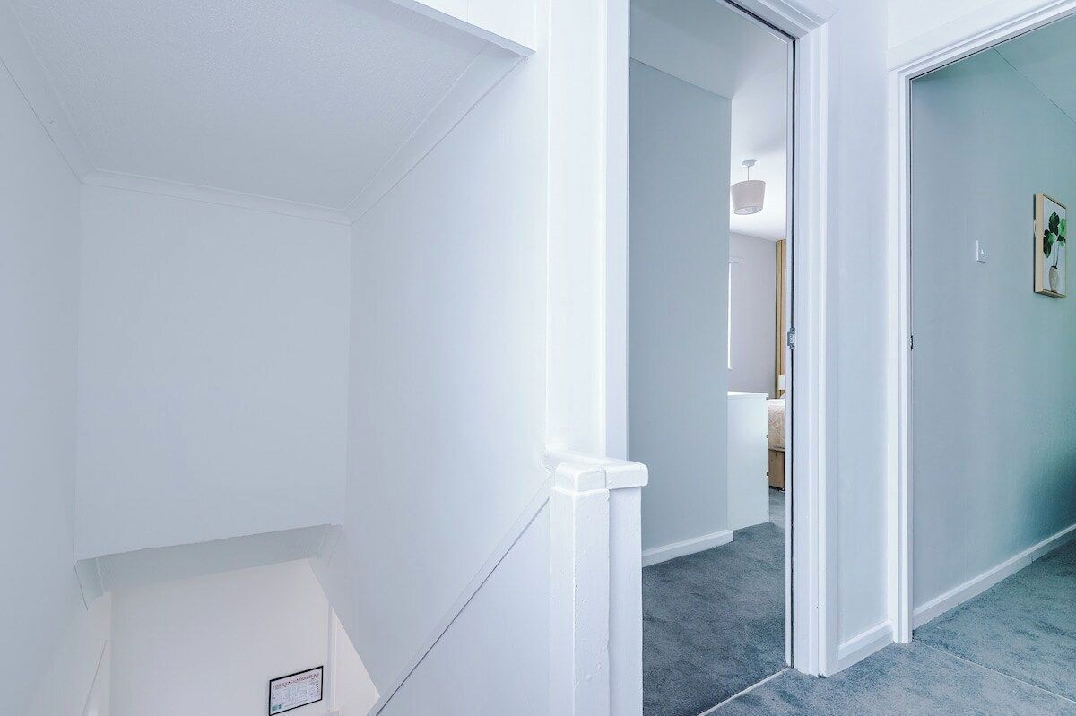 A hallway with white walls, a door leading to another room, and a carpeted floor.