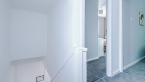 Een gang met witte muren, een deur naar een andere kamer en een vloerbedekking.