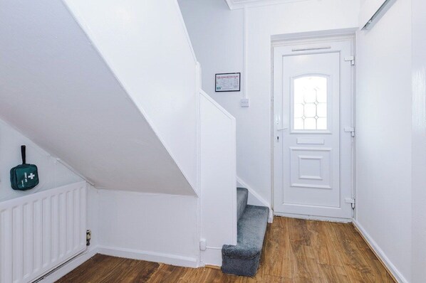 A white-walled hallway with a wooden floor, a door with a window, and a small step leading to a landing.