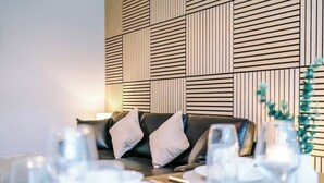 Een zithoek met een zwarte leren bank, witte kussens en een tafel gedekt met borden en glazen.