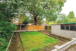 A backyard with a large tree, a wooden fence, and a small building with windows. - 2BR House By Eason Stays Short Lets Wythenshawe (Greater Manchester)