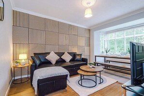 A modern living room with a black leather sofa, a wooden coffee table, and a television.