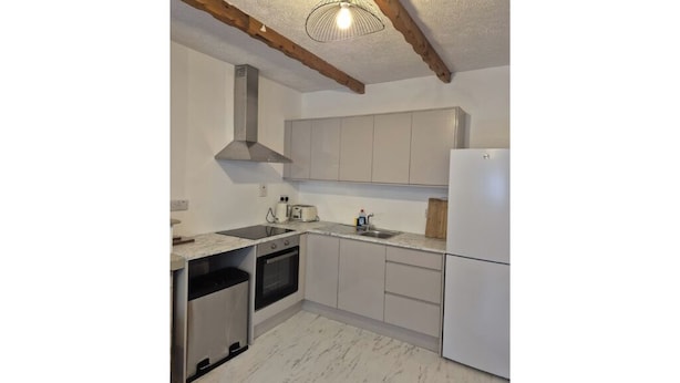 Una cocina con gabinetes blancos, una campana extractora de acero inoxidable, un horno empotrado y un lavavajillas.