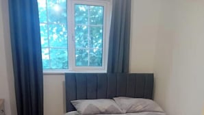 Un dormitorio con cama, ventana con cortinas y suelo de madera.