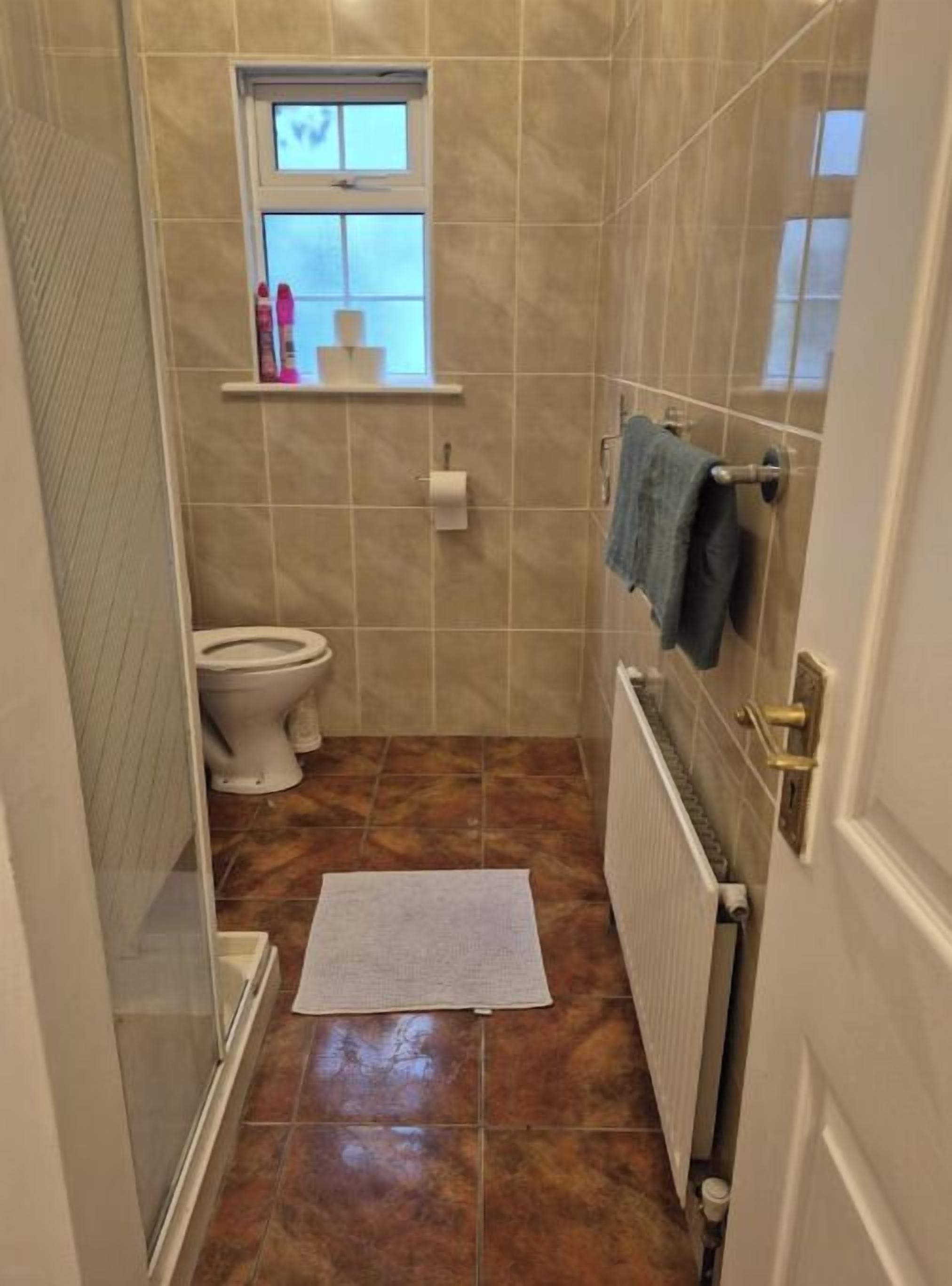 A small bathroom with a toilet, a window, a towel rack, and a radiator.