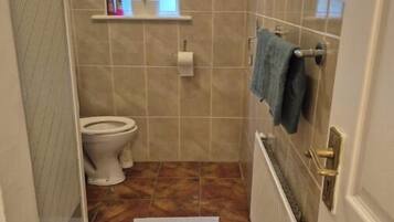 A small bathroom with a toilet, a window, a towel rack, and a radiator.