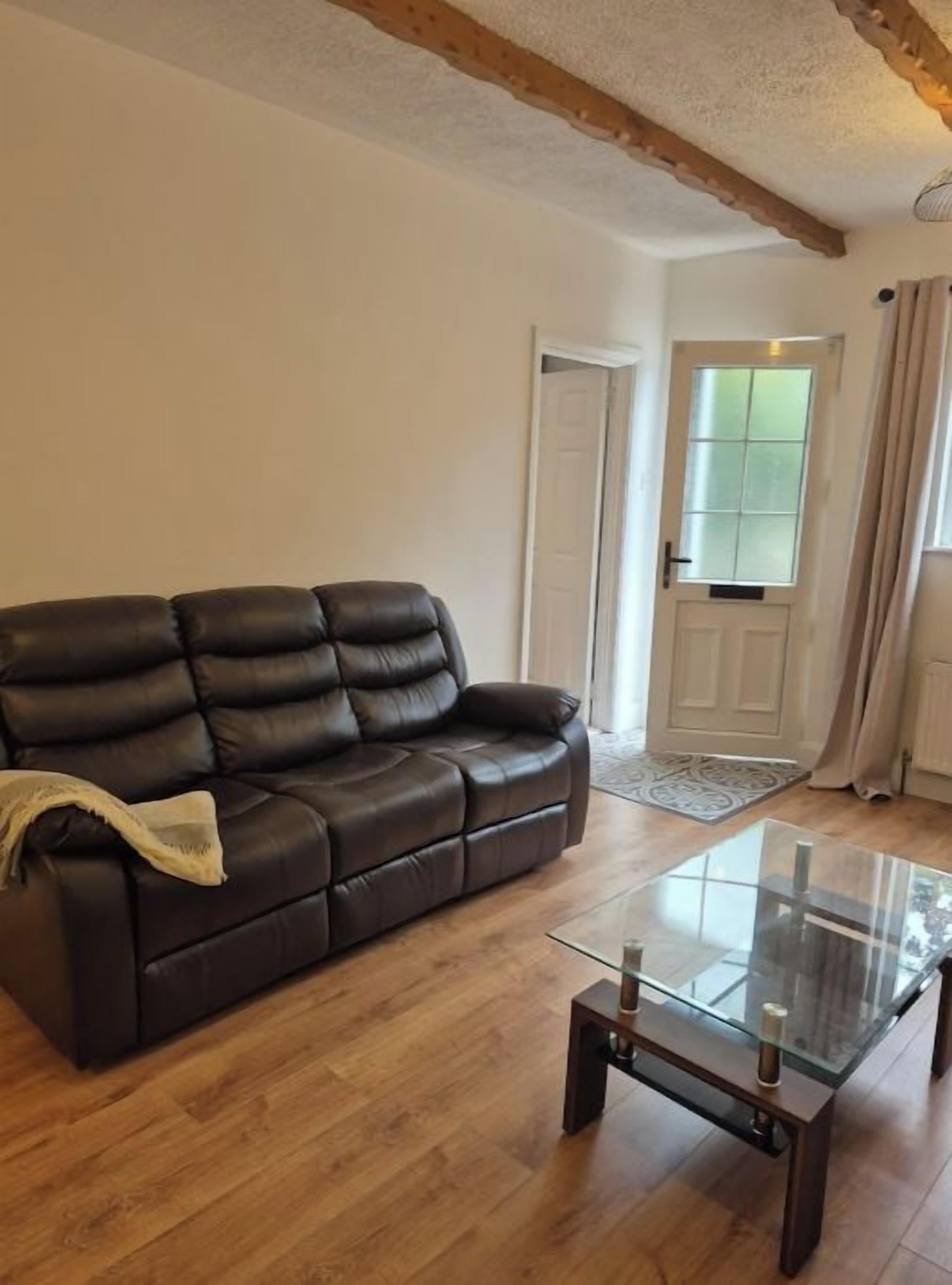 A living room with a leather sofa, a glass coffee table, wooden flooring, and a door with a window.