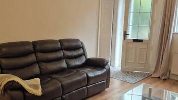 A living room with a leather sofa, a glass coffee table, wooden flooring, and a door with a window.