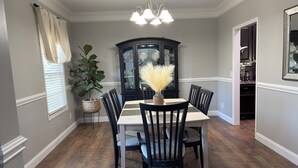 Un comedor con una mesa dispuesta para cuatro personas, rodeada de sillas, un aparador de madera oscura con puertas de cristal y una lámpara colgante.
