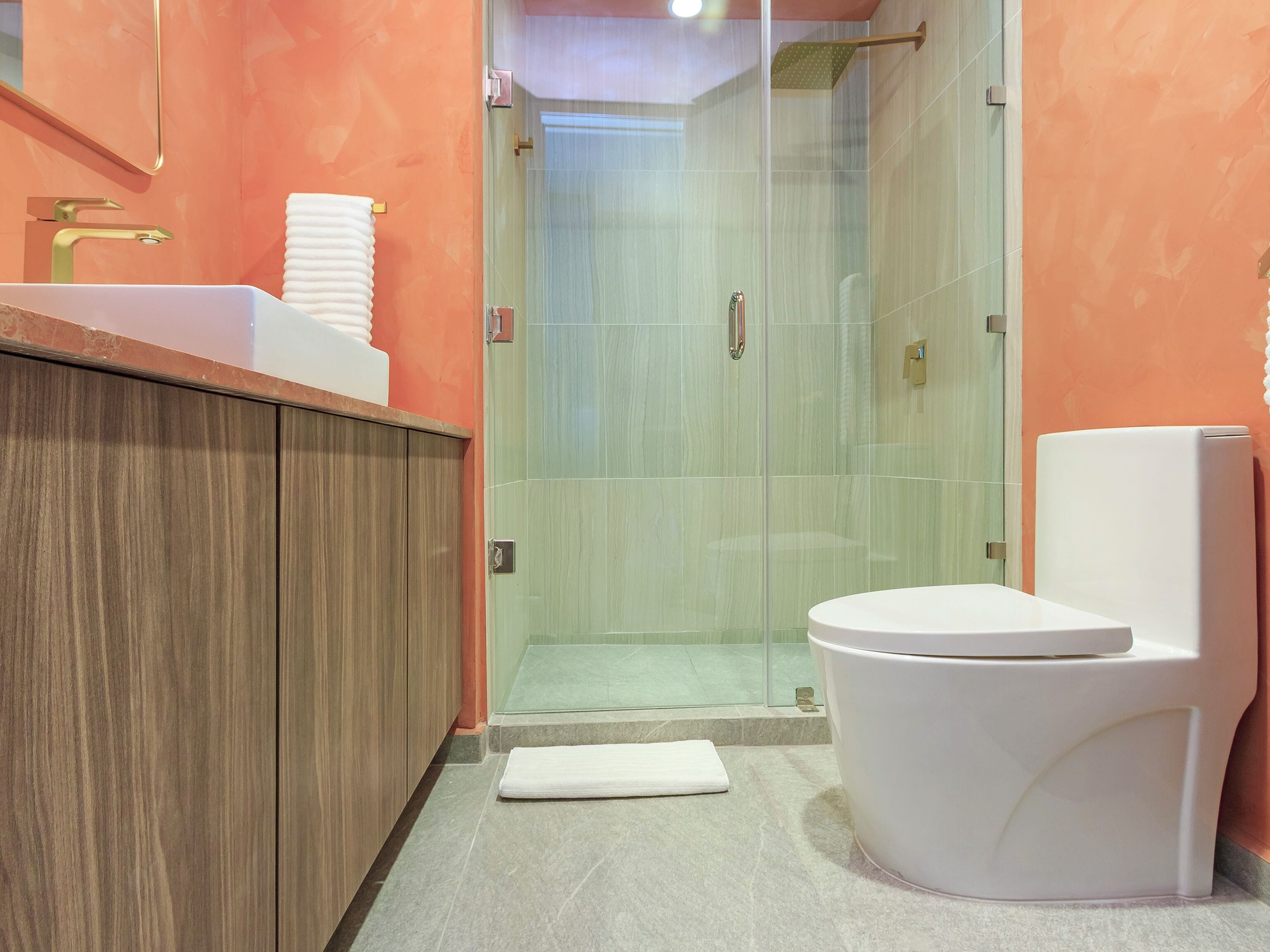Ein modernes Badezimmer mit einem Holzwaschtisch, einer weißen Toilette und einer Duschkabine aus Glas.