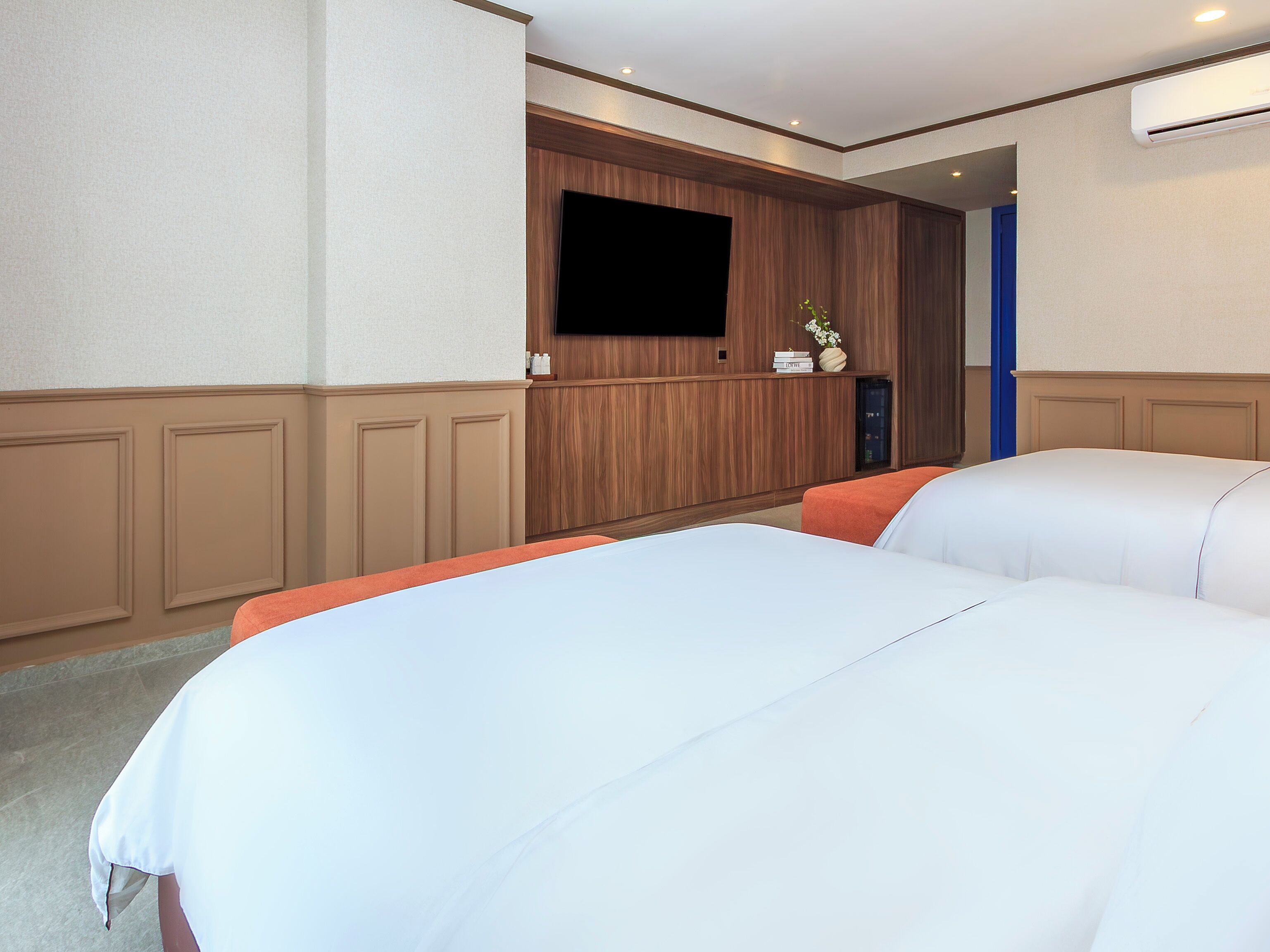 Quarto de hotel com duas camas, televisão fixada na parede e um pequeno armário com artigos de higiene pessoal.