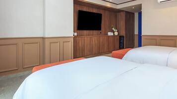 Quarto de hotel com duas camas, televisão fixada na parede e um pequeno armário com artigos de higiene pessoal.