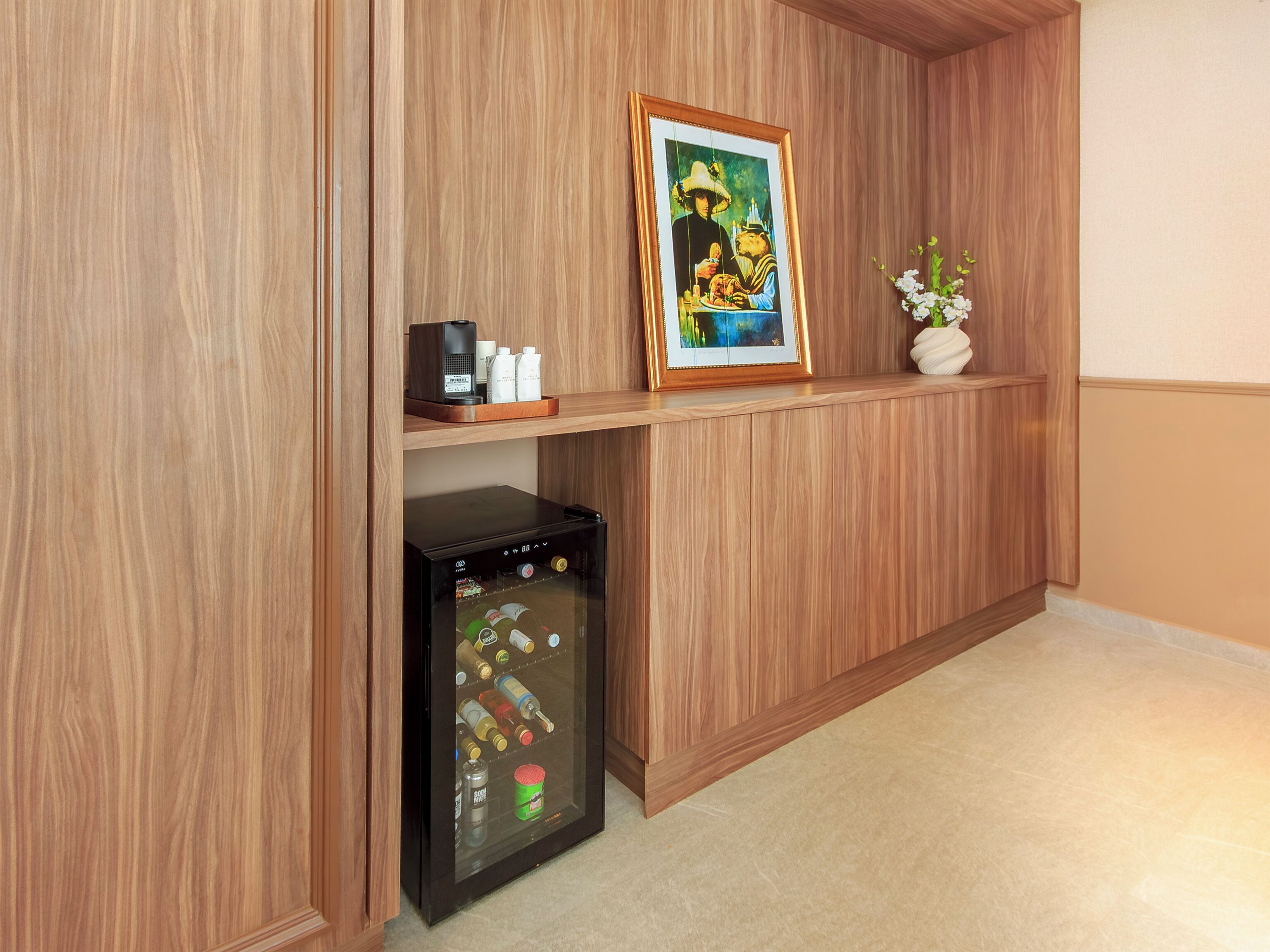 Eine Holzwand mit einem gerahmten Gemälde, einem kleinen Ablagefach mit Toilettenartikeln und einer Minibar.