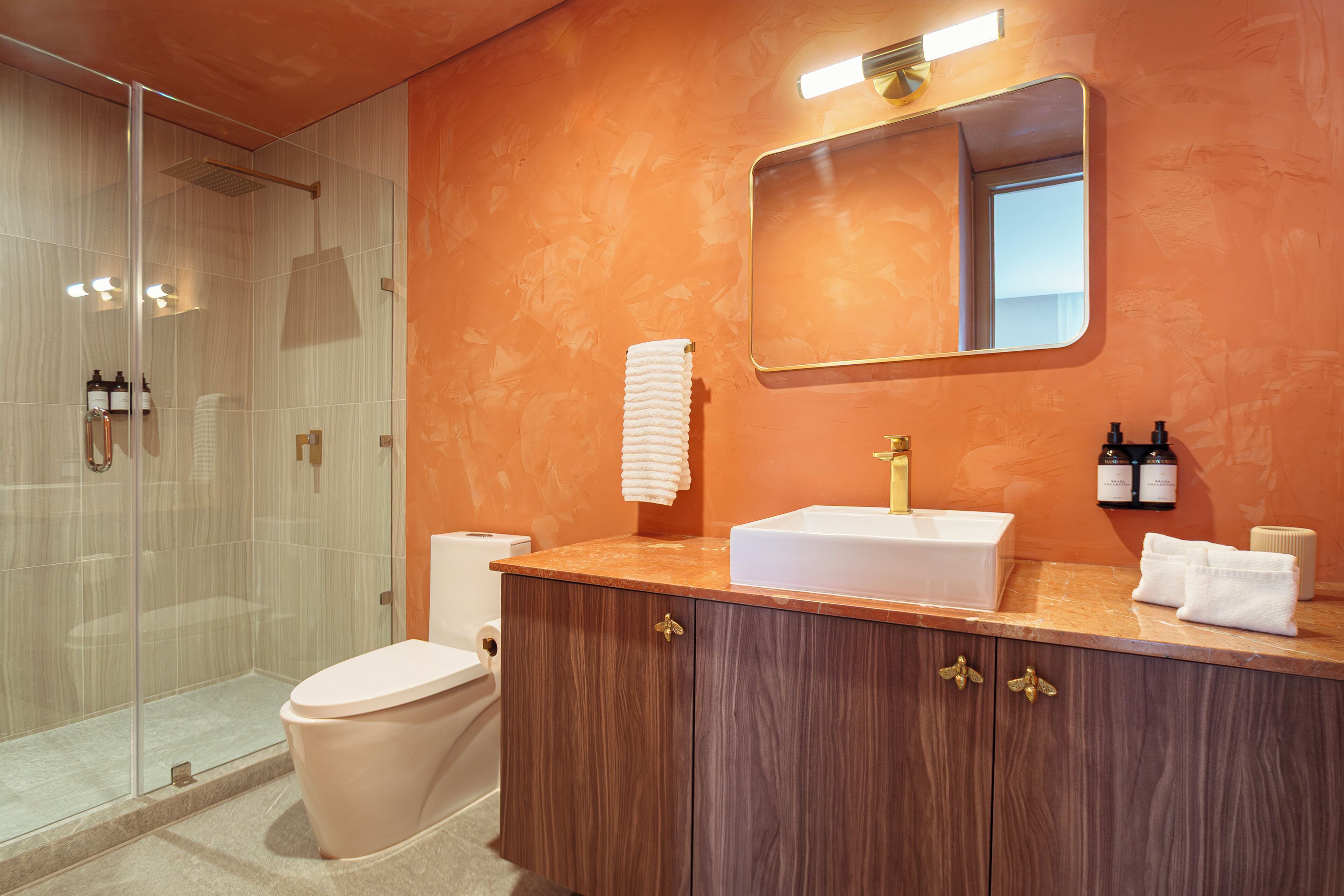 Une salle de bain avec une douche à parois de verre, des toilettes blanches, un meuble-lavabo en bois et un miroir au-dessus du meuble-lavabo.