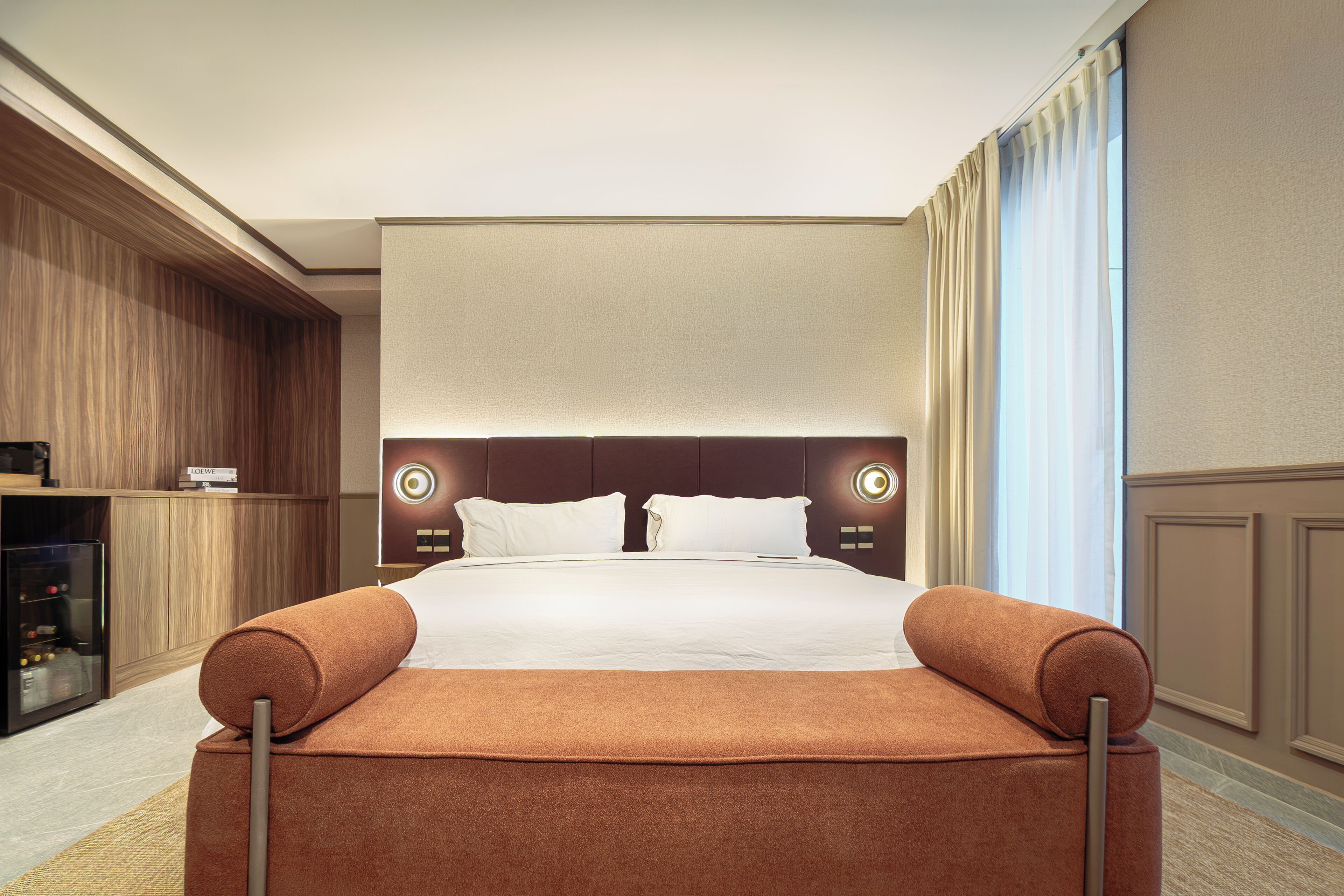 A hotel room with a large bed, a wooden wardrobe, a flat-screen TV, and a large window with curtains.