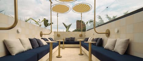 Een modern buitenzitgedeelte met banken en tafels, overdekte gestreepte parasols en een uitzicht op een gebouw op de achtergrond.
