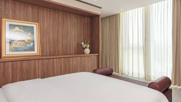 Ein Hotelzimmer mit einem großen Bett, einem gerahmten Bild an der Wand, einer Vase mit Blumen und einem Fenster mit Vorhängen.
