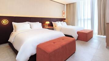 Een hotelkamer met twee bedden, een nachtkastje met lamp, een groot raam met gordijnen en een rode poef.