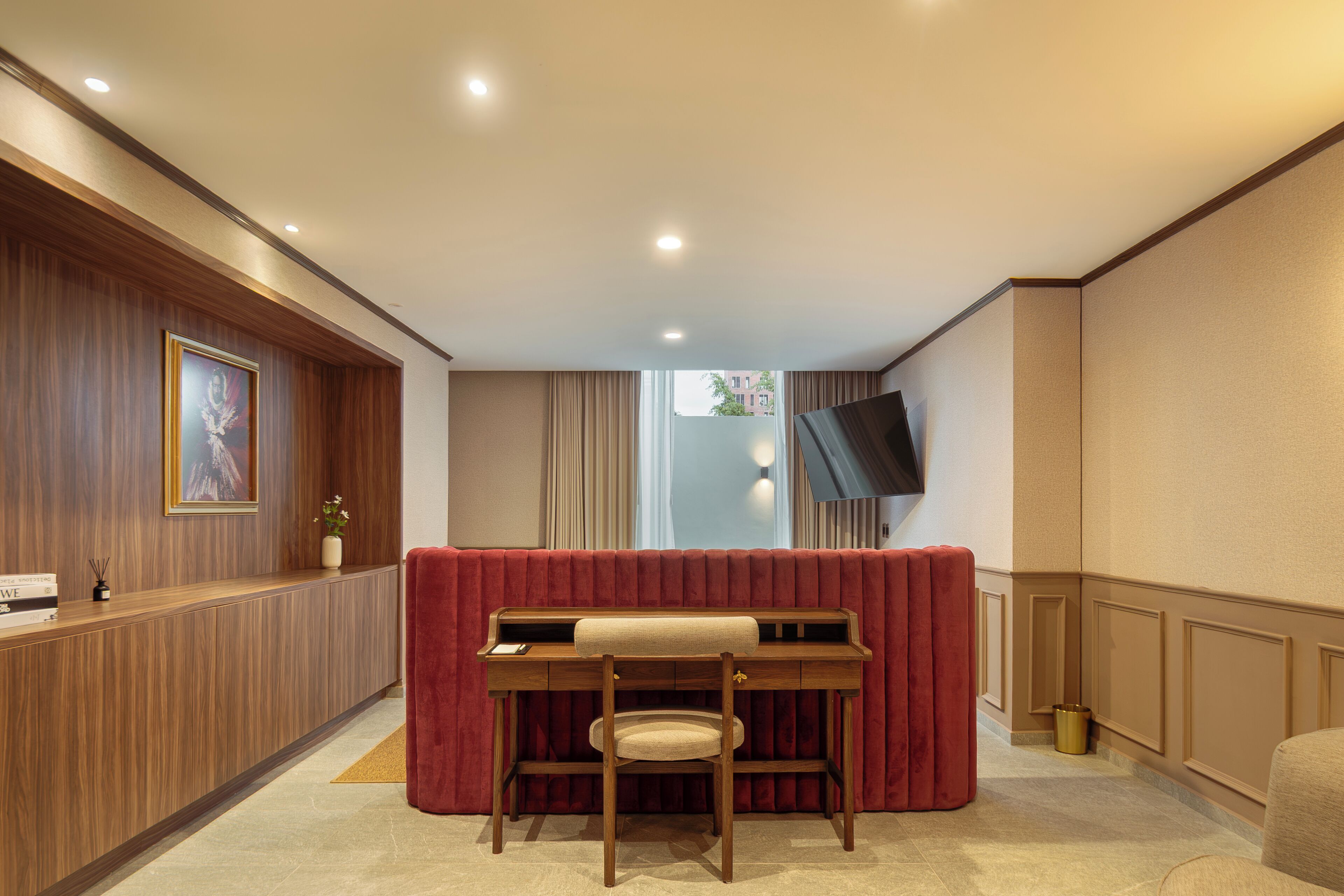 Una hall d'albergo con una reception, un divano rosso, una scrivania in legno con una sedia e un televisore a schermo piatto montato a parete.