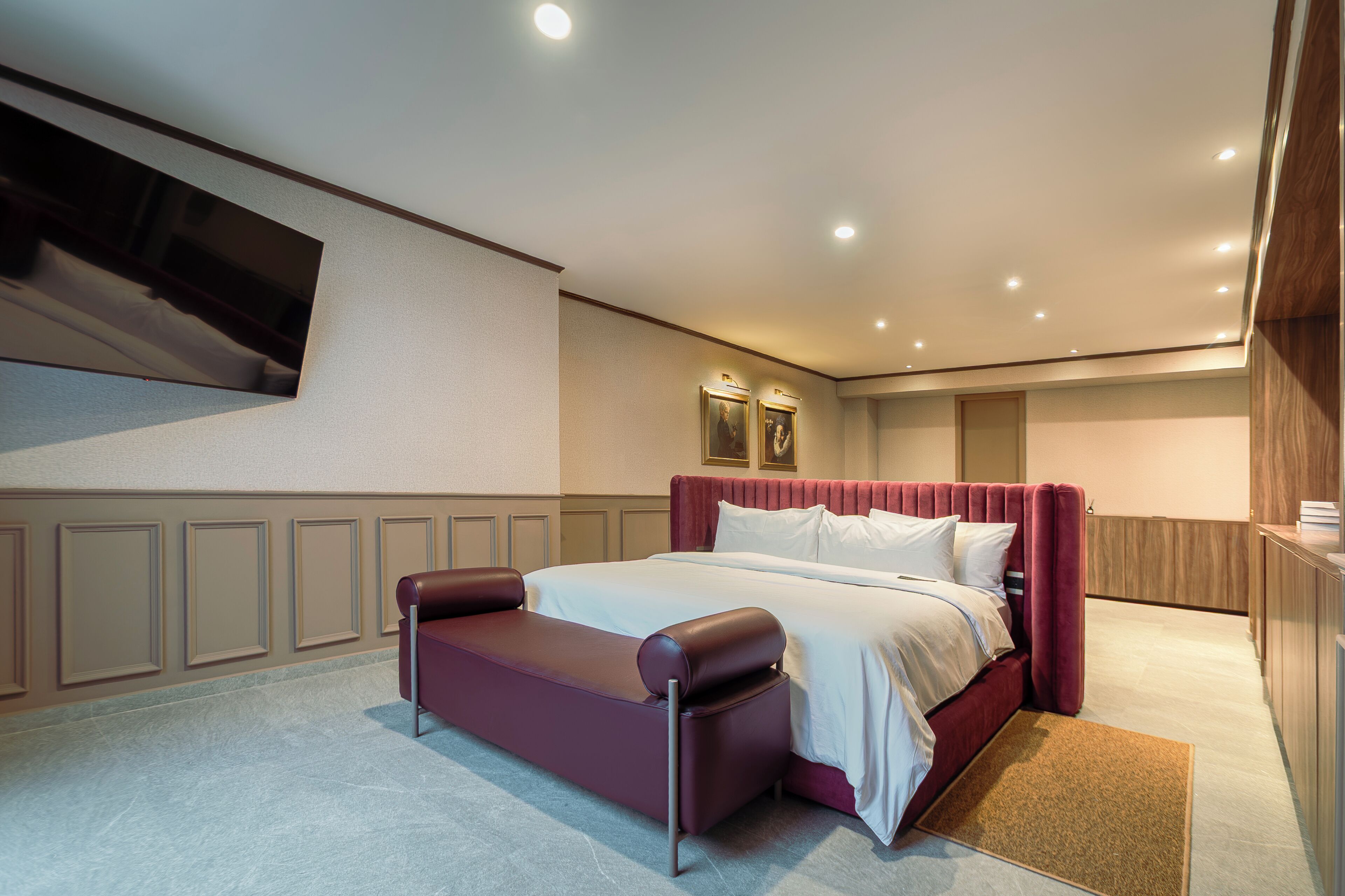 Quarto de hotel com uma cama grande, área de estar, televisão de tela plana na parede e design de painéis de madeira nas paredes.